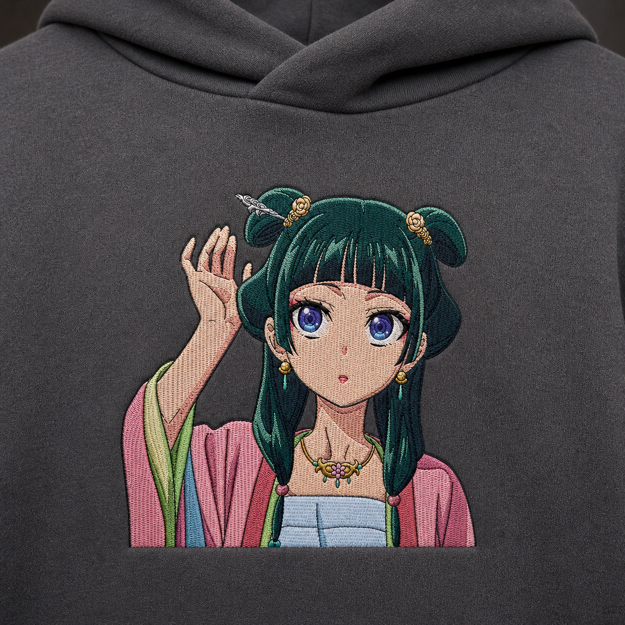 Maomao-inspired embroidered anime hoodie on dark gray cotton, detailed green hair and pink floral accents.